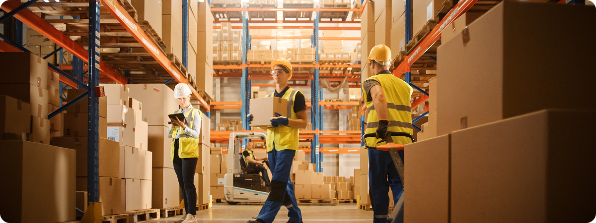 Workers wearing yellow safety vests walking around a large warehouse with packages